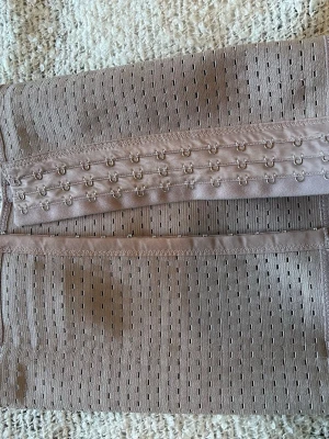 Beige midjeformare med hyskknäppning - Säljer en beige shapewear midjeformare med flera rader hyskknäppning framtill. Materialet är elastiskt och har små perforerade hål för extra andningsförmåga. Perfekt för att skapa en slät siluett under kläderna.