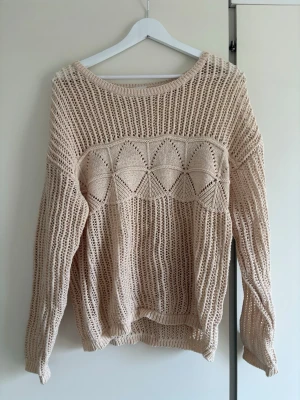 Beige stickad tröja från VILA - Säljer en beige stickad tröja från VILA i storlek L. Tröjan har ett luftigt, hålmönstrat stickat material och ett dekorativt triangelformat mönster över bröstet. Långärmad med ribbade muddar vid ärmslut och nederkant. 