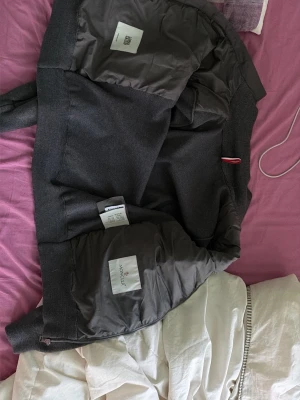 Mörkgrå pufferjacka från Moncler - Snygg mörkgrå pufferjacka från Moncler med quiltad framsida, ribbade muddar och dragkedja framtill. Jackan har två fickor med dragkedja och är tillverkad i en mix av dun och syntetmaterial. Perfekt för kalla vinterdagar och ger en clean, modern look.