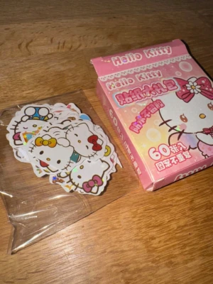 Hello Kitty klistermärken 60-pack - Säljer ett paket med 60 stycken glittriga söta Hello Kitty klistermärken i olika färger och motiv. Perfekta för att dekorera anteckningsböcker, datorer eller mobilskal. Kommer i en rosa ask med Hello Kitty-design.