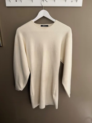 Krämvit stickad klänning från Gina Tricot - En stilren krämvit stickad klänning från Gina Tricot med rund halsringning och långa ärmar. Klänningen är gjord i ett mjukt, tjockare material som känns riktigt cozy. Perfekt att ha en sommar kväll!