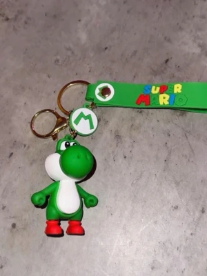 Super Mario Yoshi nyckelring - Nyckelring med Yoshi från Super Mario i grönt och vitt gummi, med röda skor och en grön rem där det står 'Super Mario' i färgglada bokstäver. Perfekt accessoar för dig som gillar gaming och Nintendo.