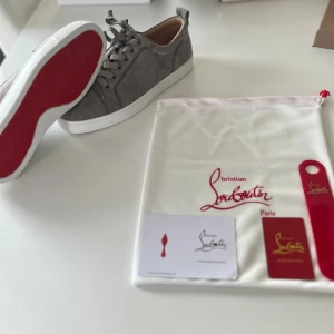 Gråa Christian Louboutin sneakers - Snygga gråa sneakers från Christian Louboutin i mocka med klassisk röd sula och vita kanter. Lågt skaft, rund tå och matchande grå skosnören. Kommer med dustbag och tillbehör. Perfekta för dig som vill ha något exklusivt och stilrent.