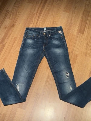 Blå jeans från Replay med slitningar - Säljer ett par feta blå jeans från Replay med slitningar och distressed detaljer på benen. Jeansen har klassisk femficksmodell, smal/anbass lik passform och snygga kontrastsömmar. Perfekta för en avslappnad och trendig look.