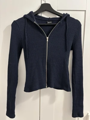 Mörkblå ribbad zipup-hoodie med dragkedja - Säljer en mörkblå ribbad zipup-hoodie från Gina Tricot med dragkedja framtill. Hoodien har långa ärmar, åtsittande passform och huva med snören. Tillverkad i ett mjukt, stretchigt material som känns skönt mot huden. Perfekt för en chill och stilren look. Skriv gärna innan ni köper❤️ Pris kan diskuteras vid snabb affär!!