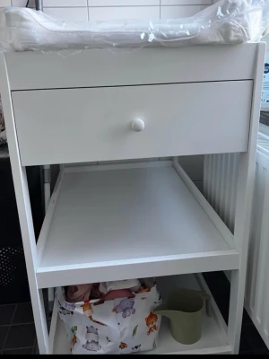 Vit skötbord med låda och hylla - Praktiskt vitt skötbord i trä med en stor låda och en öppen hylla undertill. Skötbordet har en enkel och stilren design med rundad knopp på lådan. Perfekt för att organisera blöjor och babyprodukter. Skötbädd medföljer. JLY Dream Jollyroom.