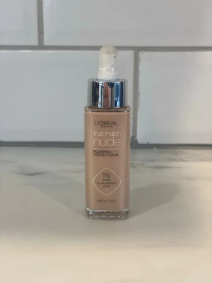 L'Oréal True Match Nude Foundation - Ljus foundation-serum från L'Oréal Paris i nyansen 1-2 Rosy Light. Kommer i en glasflaska med pipett och silverlock. Innehåller 1% hyaluronsyra för återfuktande effekt och ger en naturlig, fräsch finish.