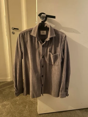 Grå manchesterskjorta med knappar - Säljer en grå manchesterskjorta från Ciszere med klassisk krage, bröstficka och knappar framtill. Skjortan har lång ärm och ett diskret randigt mönster i manchestertyget. Perfekt för dig som gillar en avslappnad men stilren look. Den är i väldigt bra skick då jag använt den sparsamt.Hör av er vid frågor!