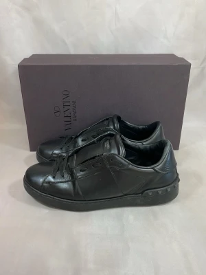 Valentino Opens Helsvarta Storlek 41 - Säljer ett par helsvarta Valentino Open sneakers i storlek 41. Endast boxen medföljer.  Skorna hade ursprungligen den klassiska VLTN-texten på sidan, men den har tagits bort. Det är inget som märks särskilt när man använder dem, men därför är priset också satt därefter.  Hör gärna av dig vid frågor eller om du vill ha fler bilder!