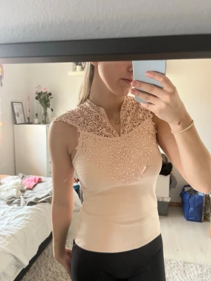 Ljusrosa spetsdetaljerad linnetopp - Linnetopp i ljusrosa med  spetsdetaljer över axlar och rygg. Toppen är ärmlös och har en v-ringning framtill. Materialet är väldigt mjukt och följsam. Storlek s, men skulle säga mer S/M