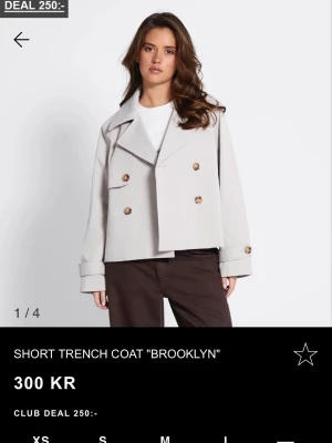 Kort trenchcoat - Kort trenchcoat i beiget med breda slag och dubbelknäppning med bruna knappar. Använd 1 gång endast