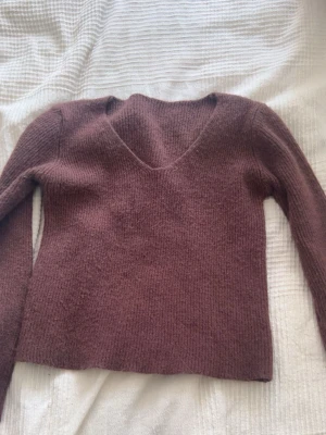 Stickad brun tröja med v-ringning - Mysig stickad tröja i en varm brun nyans. Tröjan har v-ringad hals, långa ärmar och är gjord i ett mjukt, fluffigt material. Perfekt för lager på lager och enkel att matcha med jeans eller kjol.