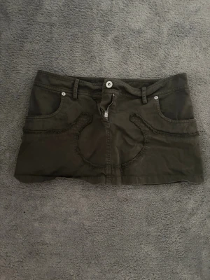 Khaki jeanskjol med fransdetaljer - Snygg khaki kortkjol med fransade detaljer och dekorativa sömmar framtill. Jättecool och köpt på second hand i köpenhamn