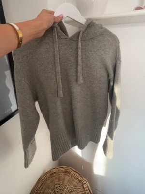 Grå hoodie i mjuk stickad kvalitet - Säljer en grå hoodie i mjuk stickad kvalitet med ribbade muddar och huva med dragsko. Perfekt för chill dagar och enkel att matcha med jeans eller mjukisbyxor. Den är från Zara i S