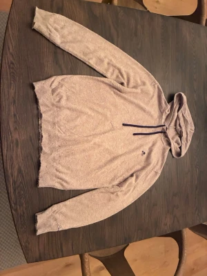 Beige hoodie från Scalpers  - Snygg beige hoodie från Scalpers med mörkblå dragsnören och den klassiska döskalle-loggan broderad på bröstet. Tillverkad i mjukt stickat material och har huva. Perfekt för en chill och avslappnad stil. Perfekt för dig som är runt 155 cm