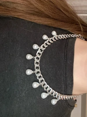 Silverfärgat halsband med pärlor - Snyggt halsband med bred silverfärgad kedja och hängande vita pärlor. Kedjan har en chunky design och pärlorna är droppformade, vilket ger ett coolt och trendigt uttryck. Perfekt för att lyfta din outfit med en unik detalj. Jag har gjort det själv!