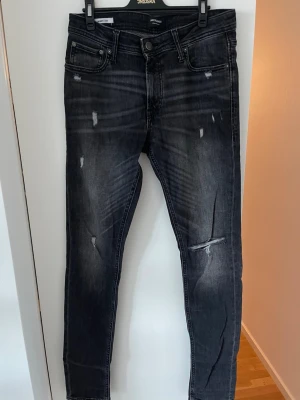 Svarta skinny jeans från Jack & Jones  - Snygga svarta skinny jeans från Jack & Jones med slitningar i modell Skinny/Liam. Storleken på jeansen är W32 L34 och har även klassisk femficksmodell, låg midja och smal passform.