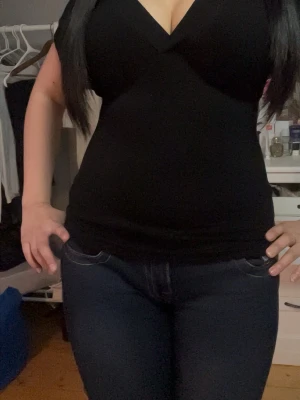 Svart v-ringad topp - Snygg svart topp med v-ringning och korta ärmar. Modellen är figurnära och har en enkel, stilren design som passar till mycket. Perfekt att matcha med jeans eller kjol för en trendig look.