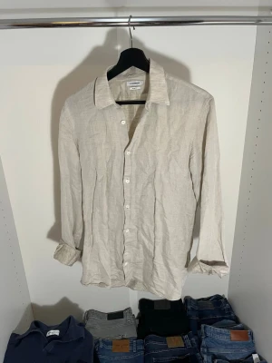 Beige linneskjorta från J.Lindeberg - Säljer en stilren beige skjorta från Lindeberg i 66% linne. Skjortan har klassisk krage, knappar framtill och långa ärmar. Hör gärna av dig vid frågor!