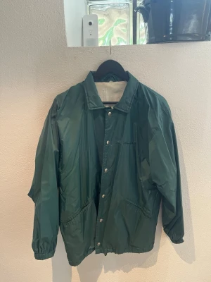 Mörkgrön vindjacka med tryckknappar - Säljer en grön jacka från Norman Wells  i storlek L. Lätt och praktisk jacka som fungerar perfekt som vindjacka eller regnjacka. Sportig modell med tryckknappar framtill och fickor. Perfekt för vardag, resa eller friluftsliv. Använd men fortfarande i bra skick. Storlek: L Märke: Norman Wells Färg: Grön Skriv gärna om du har frågor!