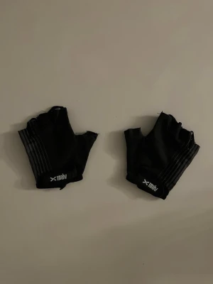 Svarta träningshandskar från Ullared  - Svarta fingerlösa träningshandskar från Ullared  med diskreta ränder och vadderad insida för extra grepp. Perfekta för gymmet eller cykling. Snygg och sportig design med logga på handleden.