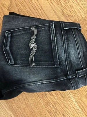 Svarta jeans från nudie  - Säljer ett par svarta jeans från nudie. Jeansen har raka ben och diskreta kontrastsömmar.  Passformen är ganska tajt midje storlek är 26. 