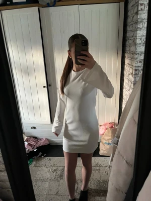 Vit långärmad kort klänning - Säljer en stilren vit kort klänning med lång ärm och snygg snörning i ryggen. Klänningen har en enkel, rak passform och är tillverkad i ett mjukt material som känns bekvämt mot huden. Perfekt för dig som gillar minimalistisk och modern stil.