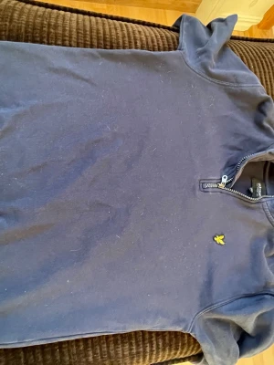 Marinblå halvzip från Lyle & Scott - Snygg marinblå långarmad pikét från Lyle & Scott Junior med halv dragkedja och klassisk gul logga på bröstet. Tröjan har en enkel design och är perfekt för en avslappnad stil. Tillverkad i mjukt material som känns skönt mot huden.