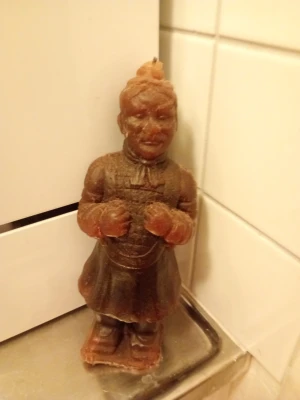 Brun soldatljus i vax - Unik ljuslykta i form av en terrakottasoldat, gjord av brunt vax. Ljusen har detaljerade drag och står upprätt med händerna framför sig. Perfekt som dekoration eller för mysig belysning hemma.