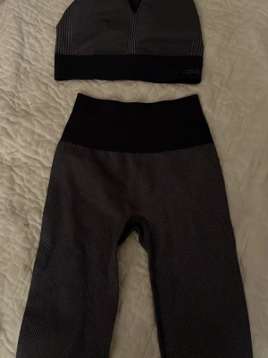 Svart/grått set från Casall - Säljer ett sportigt svart och grått set från Casall med crop top och höga tights. Setet har diskreta ränder och bred midjeresår för extra komfort. Materialet är stretchigt och följsamt, perfekt för träning eller chill. Snygg och modern design!