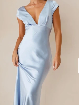 Ljusblå långklänning i satin - Elegant ljusblå långklänning i glansigt satinmaterial med djup v-ringning och öppen rygg. Klänningen har korta ärmar och figurnära passform som ger en snygg siluett. Perfekt för speciella tillfällen. Så snygg  Med frakt, tull och varan så kostade klänningen ca 1500kr (den är från Australien) Använd en gång Kolla på bilderna för detaljer och effekter Sann i storleken