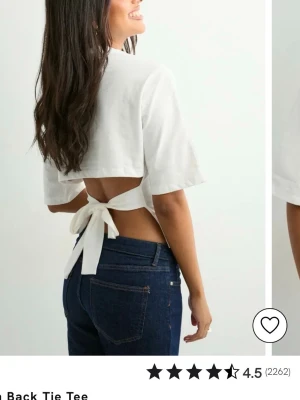 Vit croppad topp med knyt i ryggen - Trendig vit croppad topp med halvlånga ärmar och öppen rygg som knyts med breda band. Toppen har en enkel, stilren design och är perfekt för dig som vill ha en modern och luftig look. Tillverkad i mjukt bomullsmaterial.