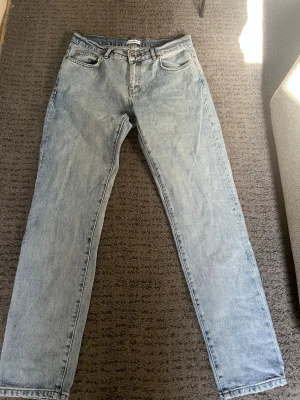 Ljusblå raka jeans från woodbird - Säljer ett par klassiska ljusblå jeans från woodbird med rak passform och hög midja. Jeansen har fem fickor, knappgylf och är tillverkade i 100% bomull för en autentisk denimkänsla. Perfekta för en avslappnad och trendig look.