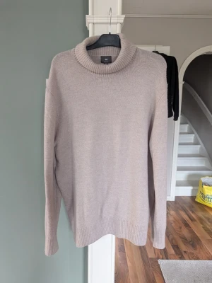 Beige polotröja från H&M - Stickad beige polotröja från H&M med lång ärm och bred ribbad krage. Tröjan har en enkel och clean design med ribbade muddar vid ärmslut och nederkant. Perfekt för lager på lager och en chill look. Aldrig använd då den inte passade mannen