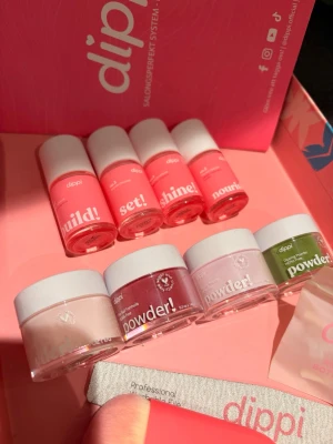 Dippi nagellack och dip powder kit - Snyggt nagelkit från Dippi med fyra flaskor nagellack i rosa toner och fyra burkar dip powder i nude, rött, ljusrosa och grönt. Inkluderar även nagelfil, borste. Perfekt för kreativa nageldesigner och trendiga färger. En burk är öppen och använd en gång, resterande är oöppnade!