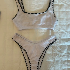 Vit bikini set med svarta detaljer från Boohoo - Snygg vit bikini set med svarta sicksack-detaljer längs kanterna från Boohoo i storlek 34. Överdelen har breda axelband och underdelen är högt skuren. Materialet är ribbat. Aldrig använda och är tvättade. 