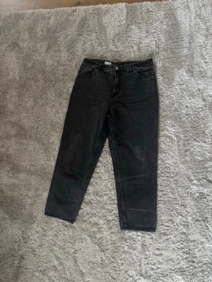 Svarta mom jeans från Monki - Säljer ett par svarta mom jeans från Monki med hög midja och raka ben. Jeansen har klassisk femficksdesign och är gjorda i kraftigt denimtyg. Perfekta för en avslappnad och trendig look.