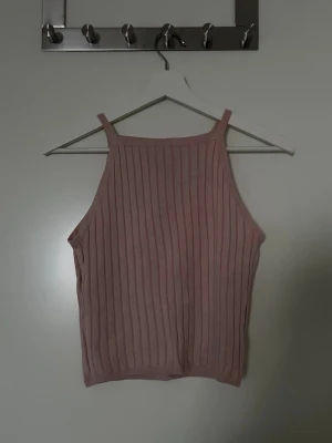 Rosa ribbad linnetopp - Säljer en ljusrosa ribbad linnetopp med smala axelband och hög halsringning. Toppen är croppad och har en mjuk, stretchig känsla. Enkel men snygg design som är lätt att matcha.