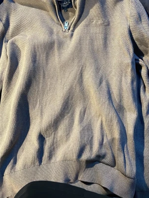 Beige halvzip tröja från Bondelid - Snygg beige tröja från Bondelid med halvzip och ståkrage. Tröjan har en diskret struktur i materialet och ribbade muddar vid ärmslut och nederkant. Perfekt för en avslappnad men stilren look. Näst intill aldrig använd