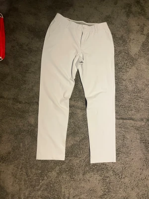 Vita golfbyxor från Under Armour - Snygga vita golfbyxor från Under Armour med klassisk rak passform och bälteshällor. Tillverkade i ett stretchigt och bekvämt material som ger bra rörelsefrihet. Perfekta för dig som vill ha en clean och stilren look.