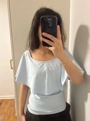Ljusblå offshoulder topp med volang XS-S - Säljer en ljusblå offshoulder topp med volang. Köpt här på Plick men inte kommit till användning! Figursydd och sitter jättefint på kroppen💞