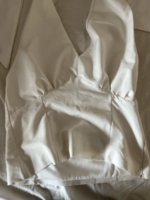 Vit halterneck festtopp - Snygg vit halterneck med djup v-ringning och figurnära passform. Toppen är ärmlös och har markerad midja som ger en smickrande siluett. Perfekt att styla med jeans eller kjol för en trendig look.
