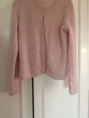 Ljusrosa kofta från Gina Tricot - Söt ljusrosa kofta från Gina Tricot med rund halsringning och långa ärmar. Koftan har knäppning framtill med matchande knappar och är gjord i ett mjukt, stickat material. Perfekt att slänga över en topp för en chill look.