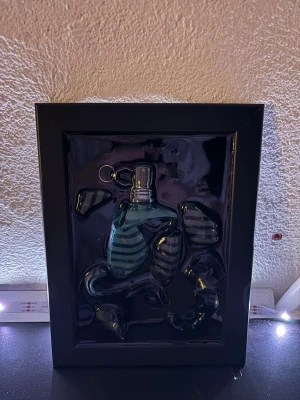 Jean Paul Gaultier Le Male parfym - Unik parfym från Jean Paul Gaultier, Le Male, i en blågrön flaska formad som en manlig torso med blå och svarta ränder. Flaskan kommer i en svart ramad förpackning som ger en cool och modern känsla.