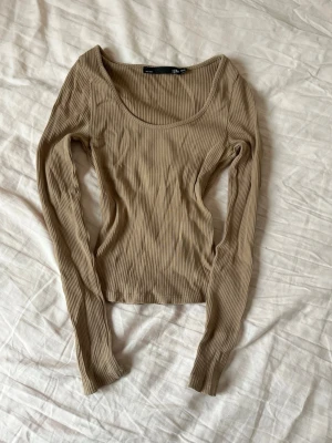 Beige ribbad långärmad topp från 157 - Säljer en beige ribbad långärmad topp från 157. Toppen har en rundad, djup urringning och är figurnära i modellen. Superfin nu till vår och sommar, passar till alla tillfällen! Aldrig använt!