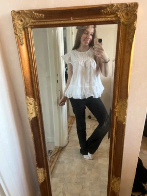 Vit volangblus med spetsdetaljer - Söt vit blus med volangkant och spetsdetaljer. Blusen har en lös passform, korta ärmar och är tillverkad i ett lätt, luftigt material som passar perfekt till varmare dagar. Enkel att styla med både jeans och kjol.