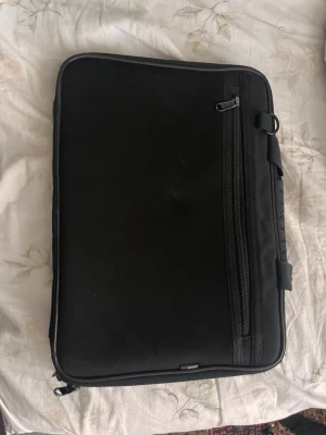 Svart datorväska  - Snygg och stilren svart datorväska från Snowcap. Väskan har en slimmad design med dragkedja runtom och ett yttre fack med dragkedja. Utrustad med bärhandtag och vadderad insida för extra skydd till din laptop.