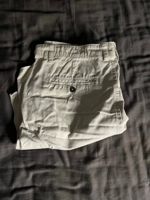 Beiga bomullsshorts med bakfickor - Stilrena beiga shorts i bomull med normal passform. Shortsen har bälteshällor och två bakfickor med knappar för en klassisk look. Perfekta för sommaren och lätta att matcha med olika outfits. I storlek s