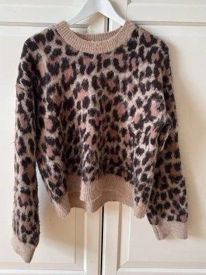 Leopardmönstrad stickad tröja - Säljer en fluffig stickad tröja med leopardmönster i beige, brunt och rosa toner. 