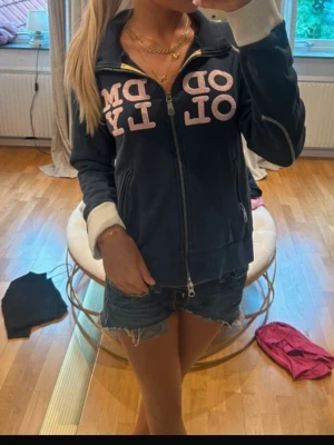 Mörkblå zip hoodie Odd Molly - Mysig mörkblå zip hoodie från Odd Molly med vita muddar och dragkedja framtill. Stora rosa bokstäver på bröstet och två fickor. Perfekt för en avslappnad och cool stil.